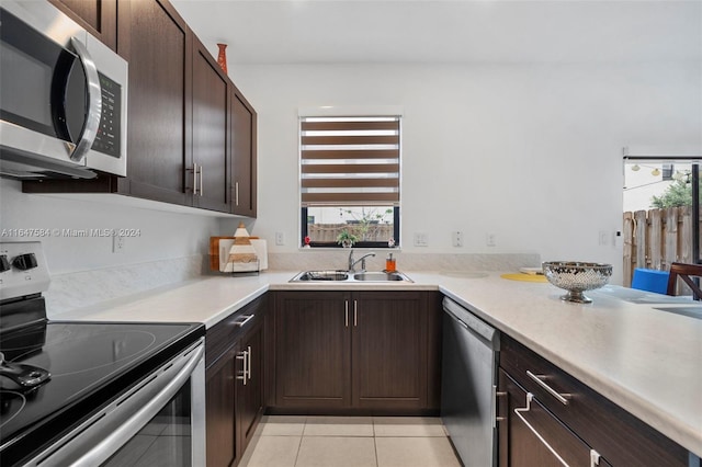 kitchen featuring dark brown cabinets, a sink, light tile patterned flooring, a healthy amount of sunlight, and stainless steel appliances