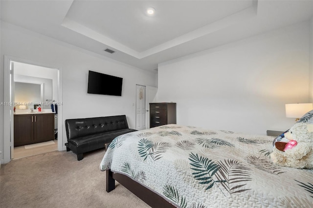 bedroom with ensuite bath, light carpet, a tray ceiling, and visible vents