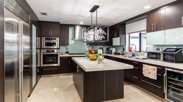 kitchen with wall chimney range hood, sink, wine cooler, a kitchen island, and stainless steel appliances