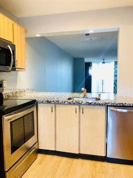 kitchen with sink, stainless steel appliances, light hardwood / wood-style floors, and light stone countertops