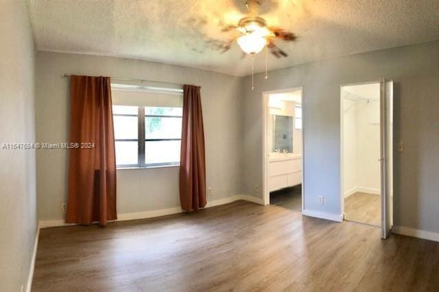 unfurnished bedroom with ceiling fan, a spacious closet, wood-type flooring, ensuite bathroom, and a textured ceiling