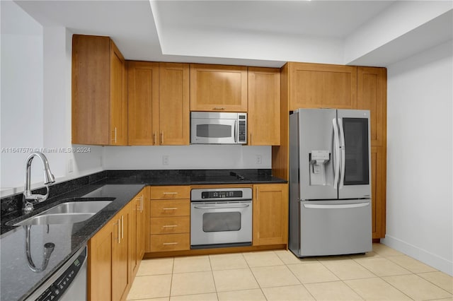 kitchen with dark stone counters, light tile patterned flooring, stainless steel appliances, and sink