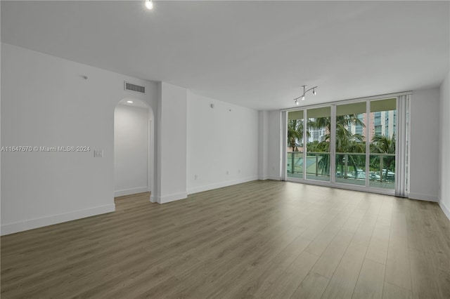 empty room featuring floor to ceiling windows, light wood-type flooring, and track lighting