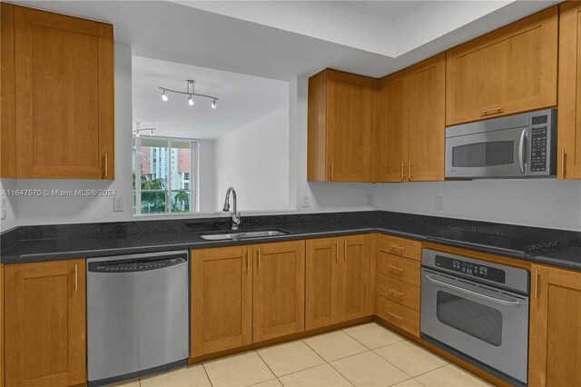 kitchen with dark stone counters, track lighting, light tile patterned floors, stainless steel appliances, and sink