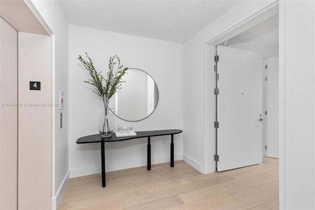corridor with elevator, baseboards, and light wood finished floors