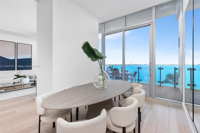 dining area featuring a water view, a wall of windows, and light wood-style floors