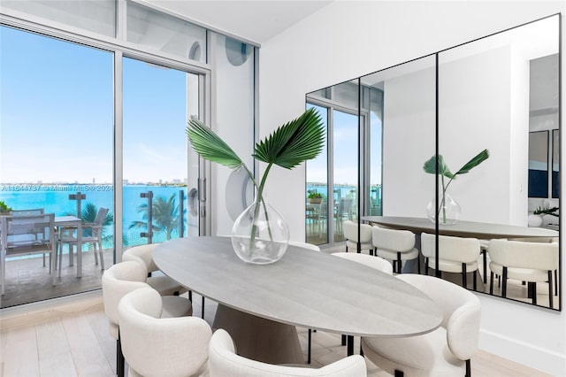 dining area with a wealth of natural light, light hardwood / wood-style flooring, a water view, and expansive windows