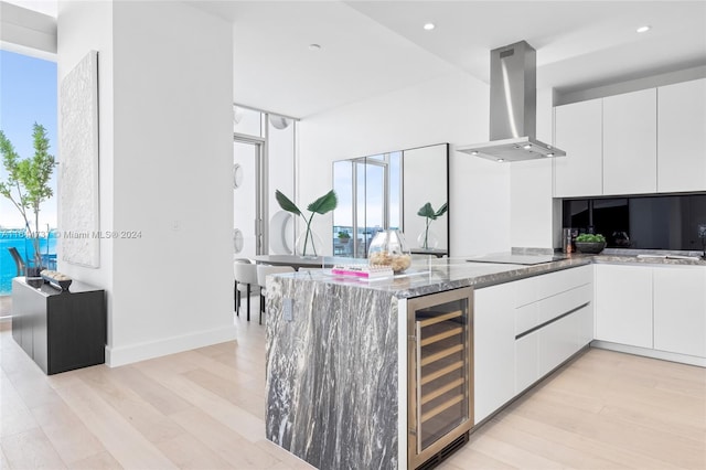 kitchen featuring island exhaust hood, light wood-type flooring, stone countertops, white cabinets, and beverage cooler