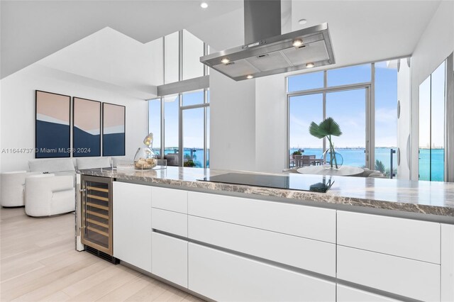 kitchen with island exhaust hood, light stone countertops, black electric cooktop, beverage cooler, and white cabinetry