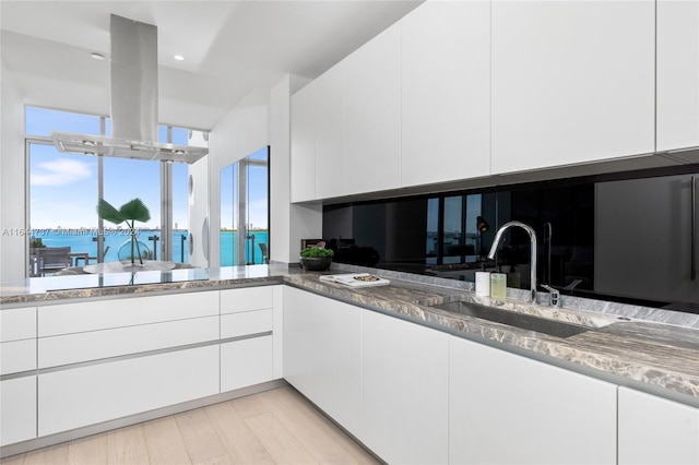 kitchen featuring white cabinetry, island range hood, black electric stovetop, and a sink