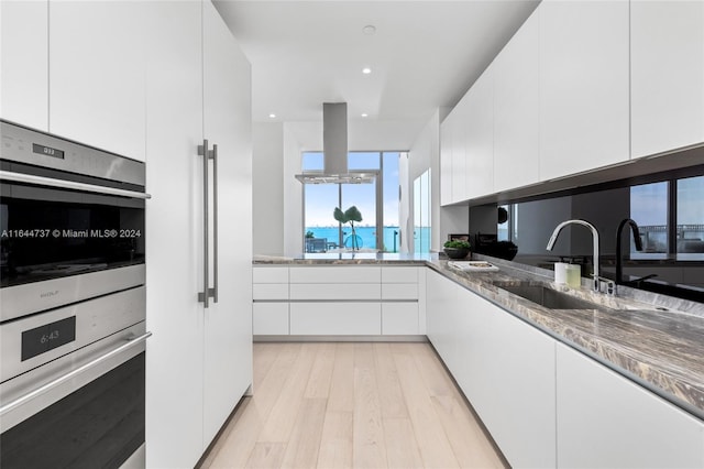 kitchen featuring double oven, sink, white cabinetry, and light hardwood / wood-style flooring