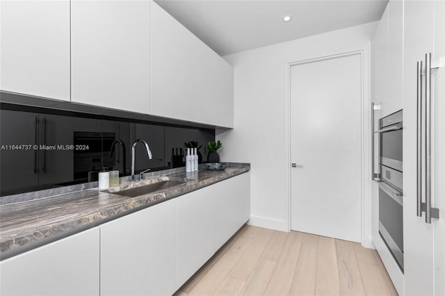 kitchen featuring sink, stainless steel oven, white cabinetry, and light hardwood / wood-style floors