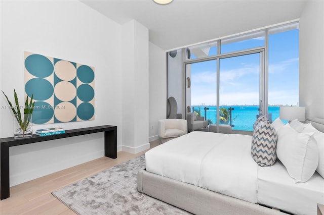 bedroom with wood finished floors, a wall of windows, baseboards, access to exterior, and a water view