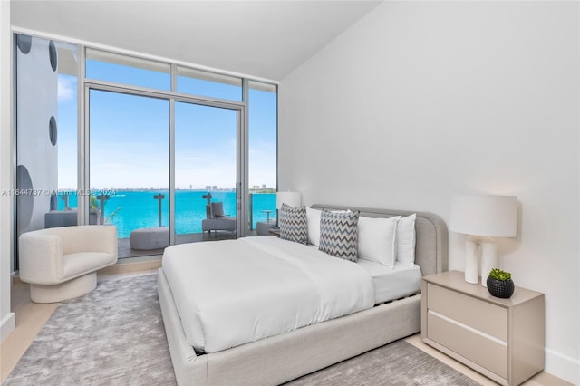 bedroom with a water view, baseboards, floor to ceiling windows, and wood finished floors
