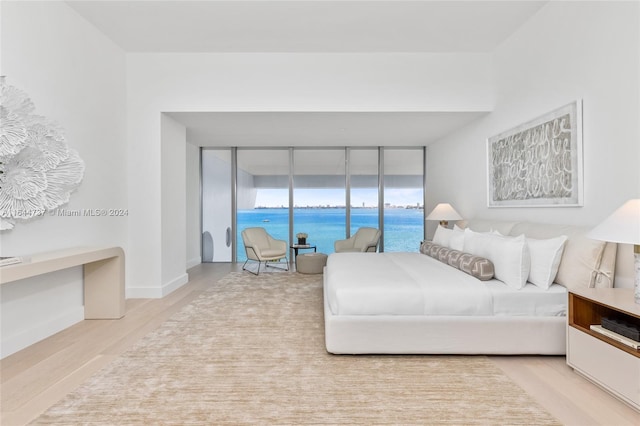 bedroom with a water view, floor to ceiling windows, access to exterior, and light hardwood / wood-style flooring