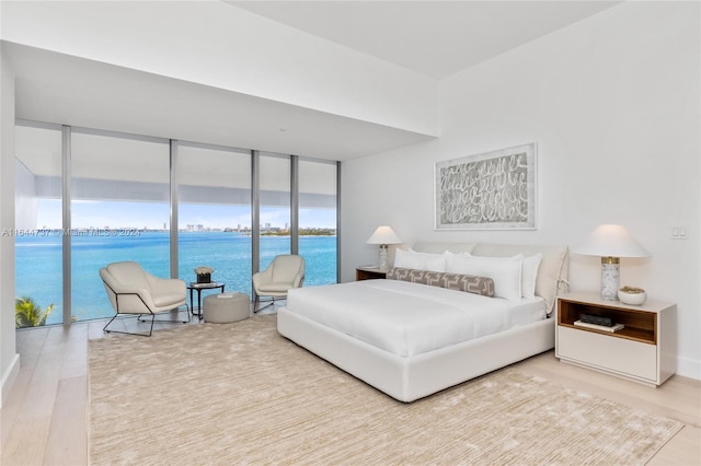 bedroom with expansive windows, a water view, and wood finished floors