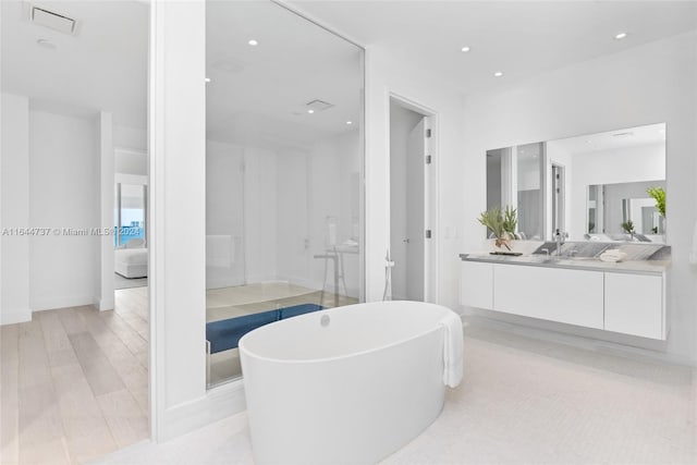 ensuite bathroom with vanity, wood finished floors, ensuite bathroom, recessed lighting, and a soaking tub