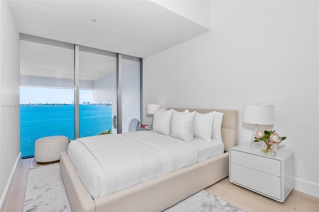 bedroom featuring light hardwood / wood-style flooring, a water view, and access to outside