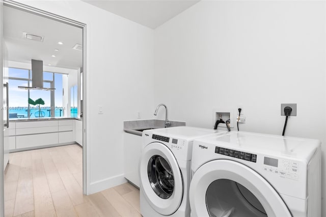 laundry area featuring washer and dryer, cabinets, sink, and light hardwood / wood-style floors