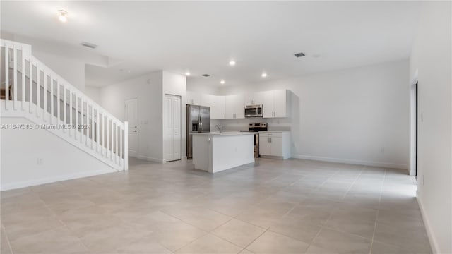 kitchen featuring light tile patterned flooring, sink, white cabinetry, stainless steel appliances, and a center island with sink