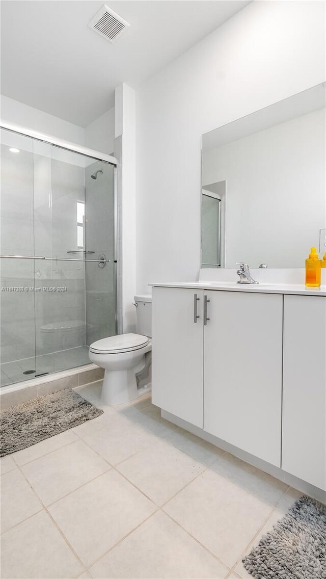 bathroom featuring a shower with door, toilet, vanity, and tile patterned floors