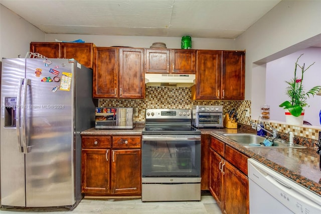 kitchen featuring sink, dark stone countertops, appliances with stainless steel finishes, light hardwood / wood-style flooring, and tasteful backsplash