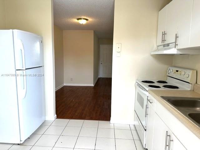 kitchen featuring light wood-type flooring, a textured ceiling, white appliances, and white cabinets