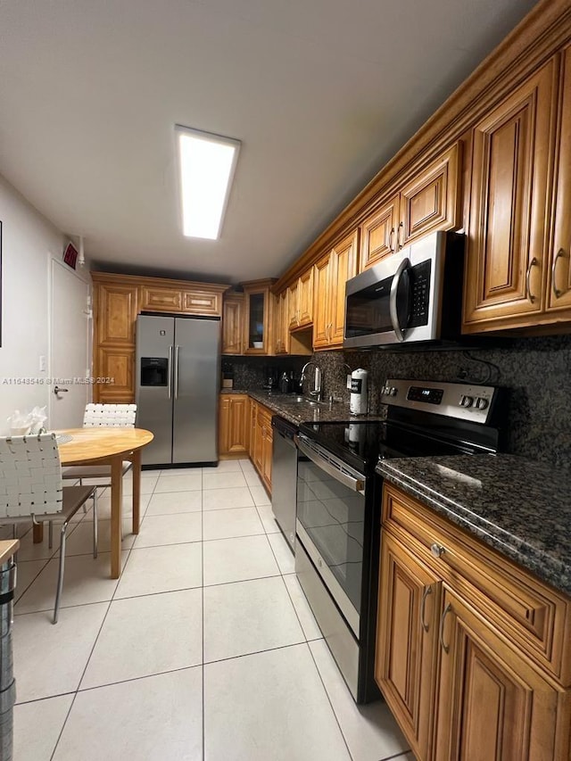 kitchen featuring appliances with stainless steel finishes, light tile patterned floors, dark stone countertops, and tasteful backsplash