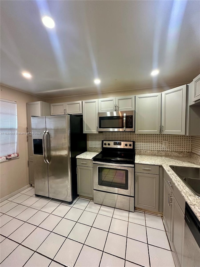 kitchen featuring backsplash, stainless steel appliances, sink, light stone counters, and light tile patterned flooring