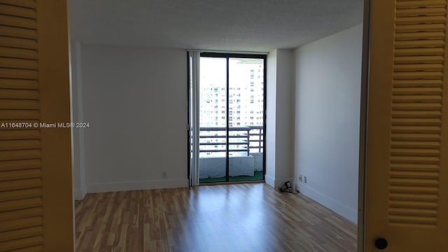 unfurnished room with a textured ceiling, hardwood / wood-style floors, and a wall of windows