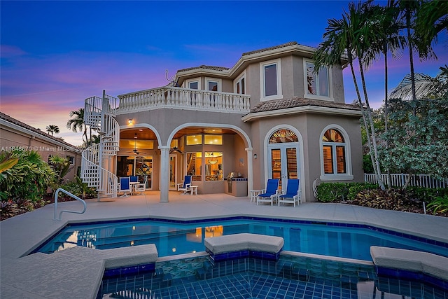 back house at dusk featuring a patio, a balcony, and a pool with hot tub