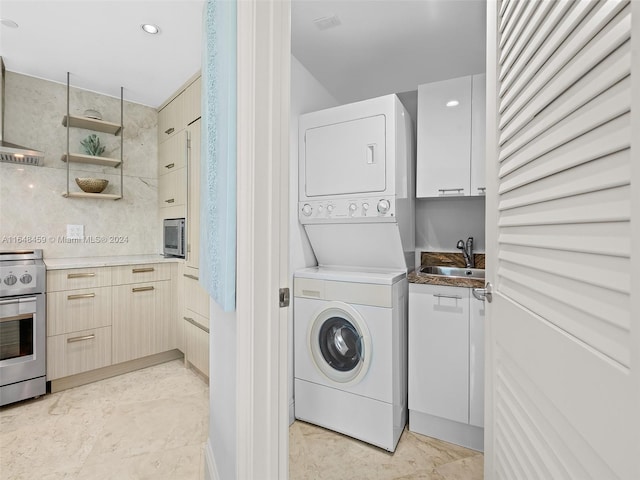 clothes washing area featuring stacked washer / drying machine, light tile patterned floors, and sink