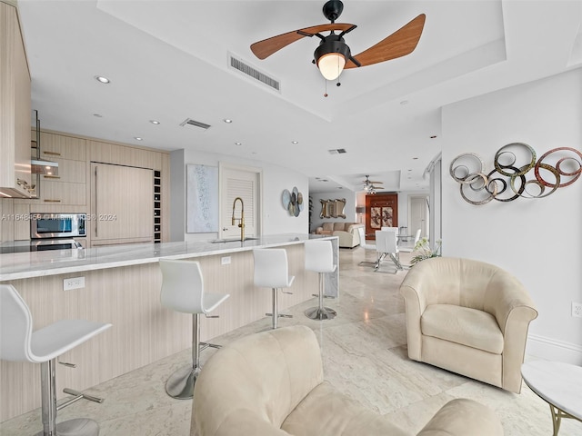 living room featuring ceiling fan, a raised ceiling, and sink