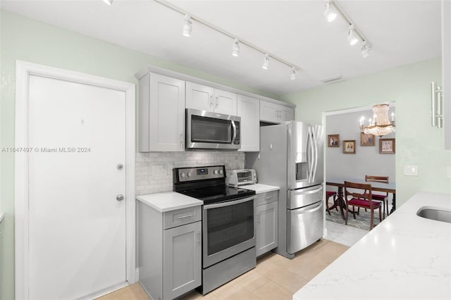 kitchen with an inviting chandelier, rail lighting, decorative backsplash, light stone countertops, and stainless steel appliances