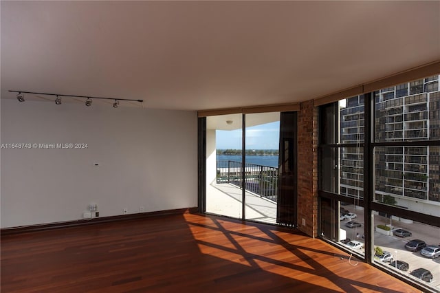 empty room featuring hardwood / wood-style flooring, track lighting, floor to ceiling windows, and a water view