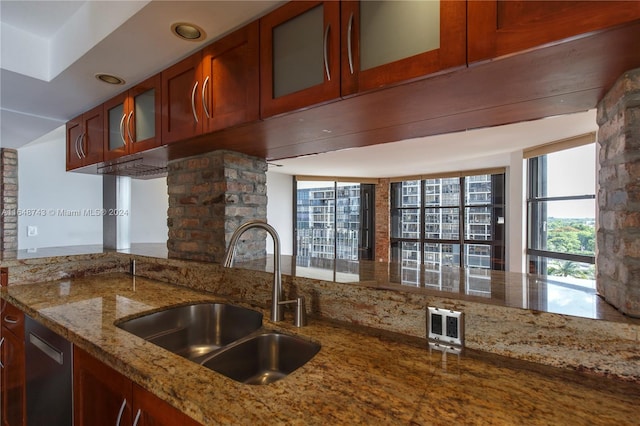 kitchen with expansive windows, stainless steel dishwasher, sink, light stone counters, and kitchen peninsula