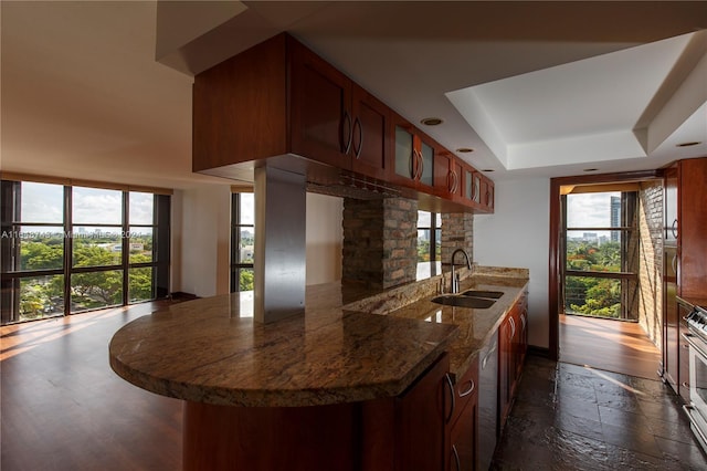 kitchen with dark hardwood / wood-style flooring, a tray ceiling, range, sink, and kitchen peninsula