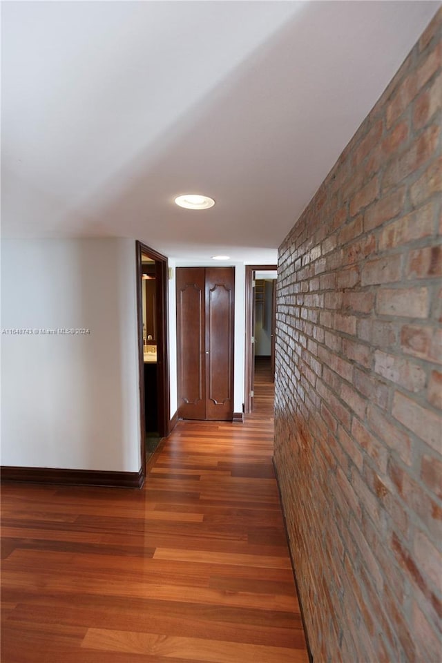 hallway featuring brick wall and wood-type flooring