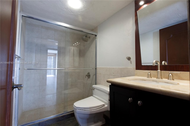 bathroom with tile walls, toilet, an enclosed shower, and vanity