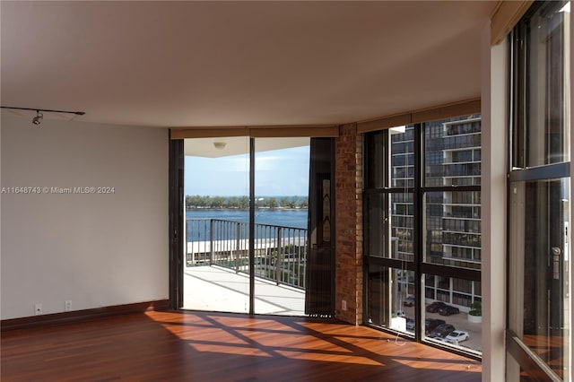 spare room featuring a wall of windows, brick wall, hardwood / wood-style floors, and a water view