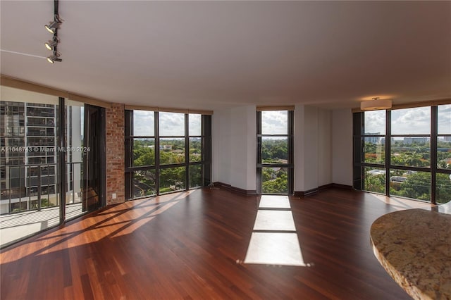 empty room featuring a wall of windows, brick wall, dark hardwood / wood-style flooring, and rail lighting