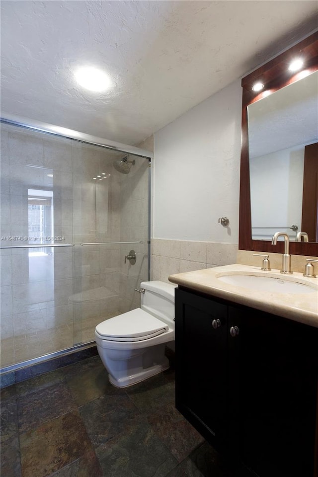 bathroom featuring tile walls, toilet, vanity, and a shower with door