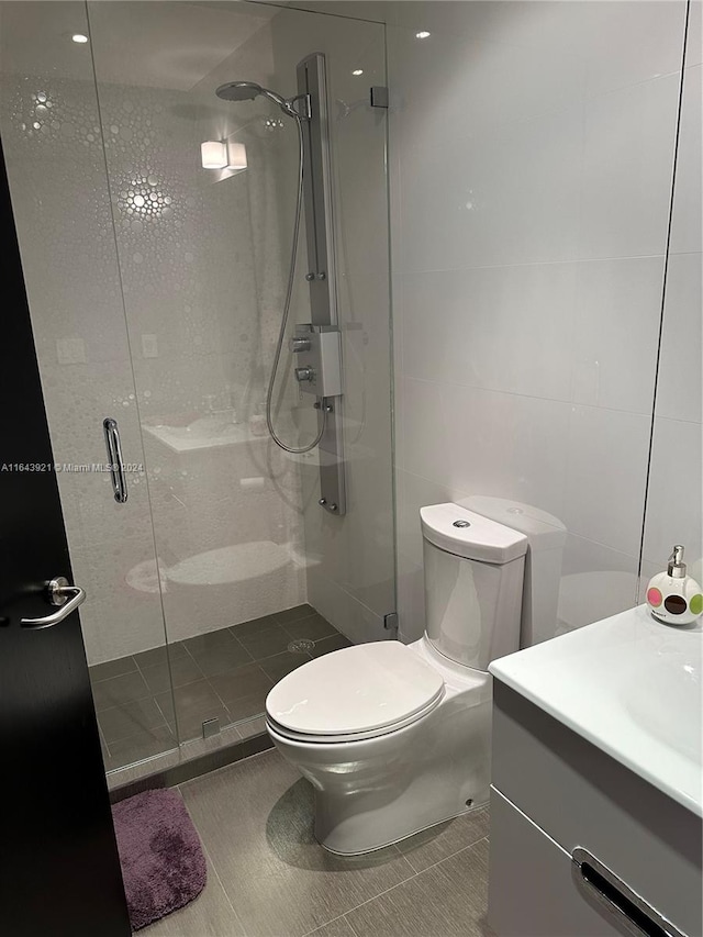 bathroom featuring vanity, toilet, tile walls, tile patterned flooring, and a shower with door