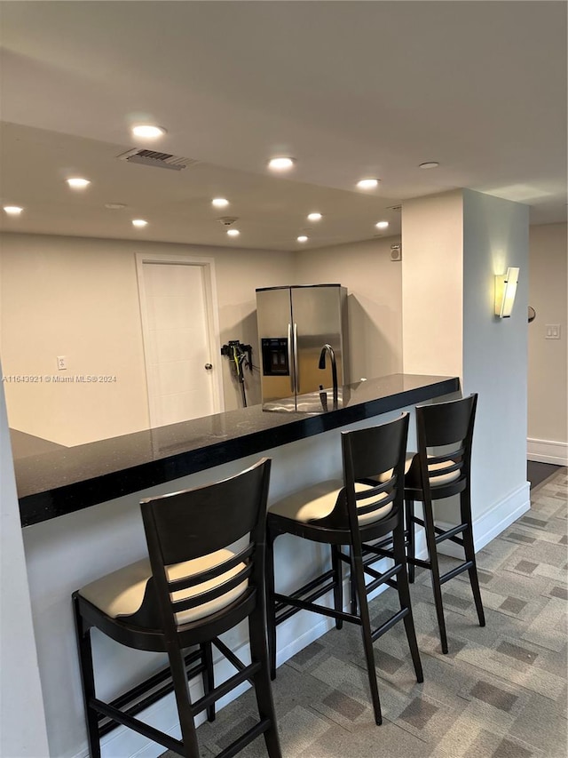 bar featuring carpet, sink, and stainless steel fridge with ice dispenser