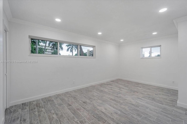 basement with light wood-type flooring, crown molding, and plenty of natural light