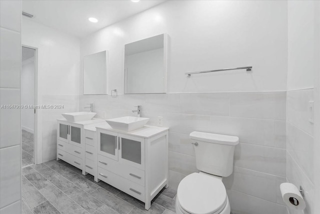 bathroom featuring toilet, vanity, and tile walls