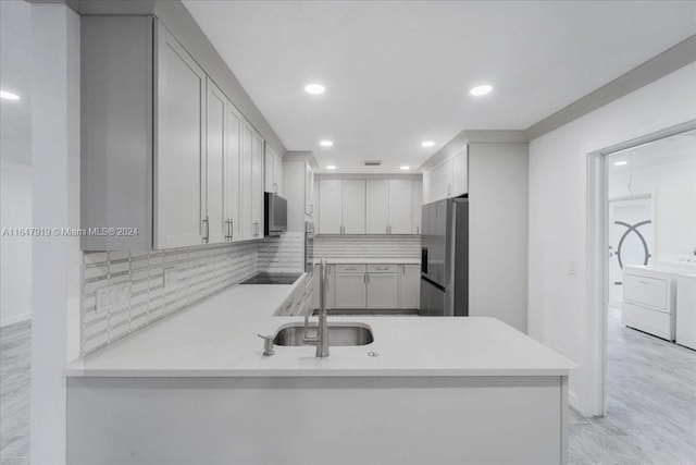 kitchen with appliances with stainless steel finishes, sink, kitchen peninsula, washer and clothes dryer, and light hardwood / wood-style flooring