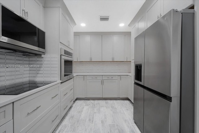 kitchen featuring white cabinets, stainless steel appliances, light wood-type flooring, and backsplash