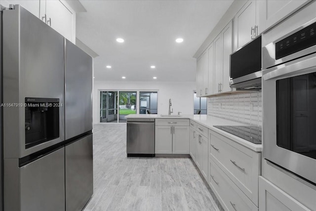 kitchen featuring tasteful backsplash, appliances with stainless steel finishes, sink, white cabinets, and light hardwood / wood-style flooring