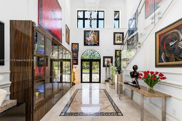 foyer entrance featuring a towering ceiling, a notable chandelier, french doors, and light tile patterned floors